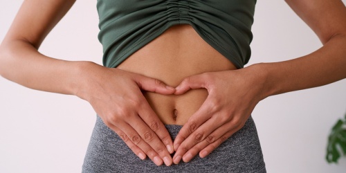 Person in athletic wear placing hands in heart shape over stomach area, representing digestive health and wellness