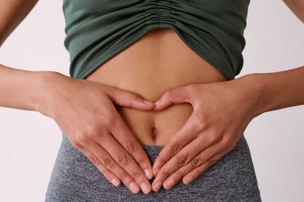 Person in athletic wear placing hands in heart shape over stomach area, representing digestive health and wellness